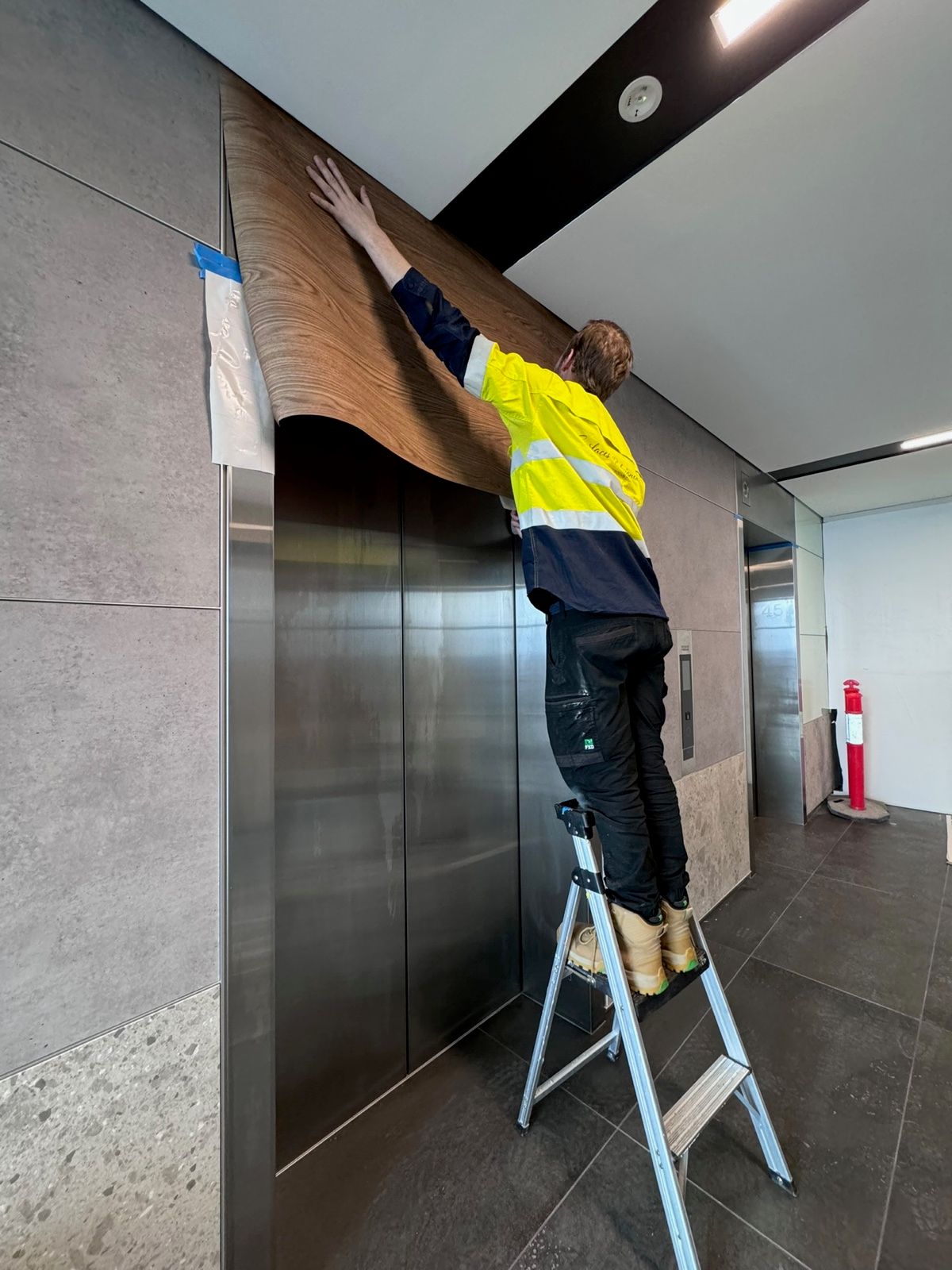 Installation in progress: Lift doors and frame, stainless to timber woodgrain